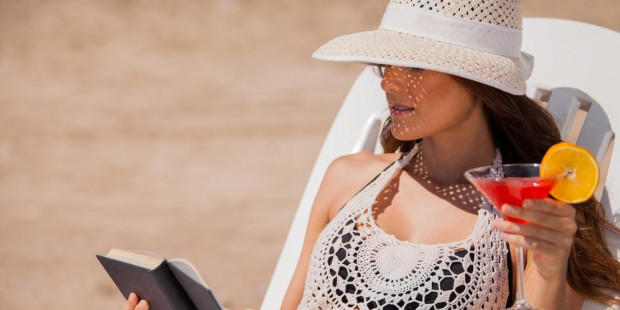 Devojka čita knjigu na plaži dok pije koktel